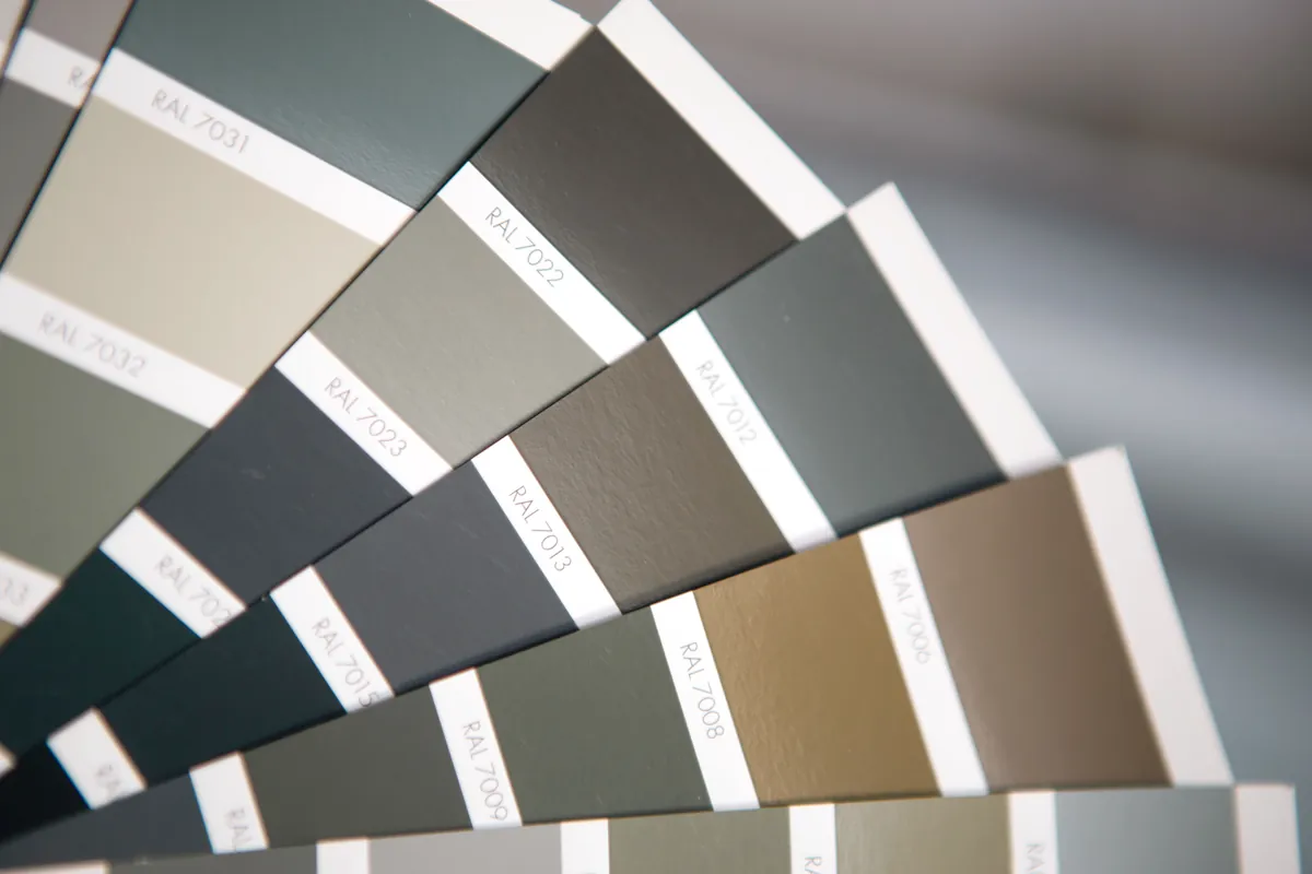 A colour fan deck held open against a wall to compare shades in the room's own light.