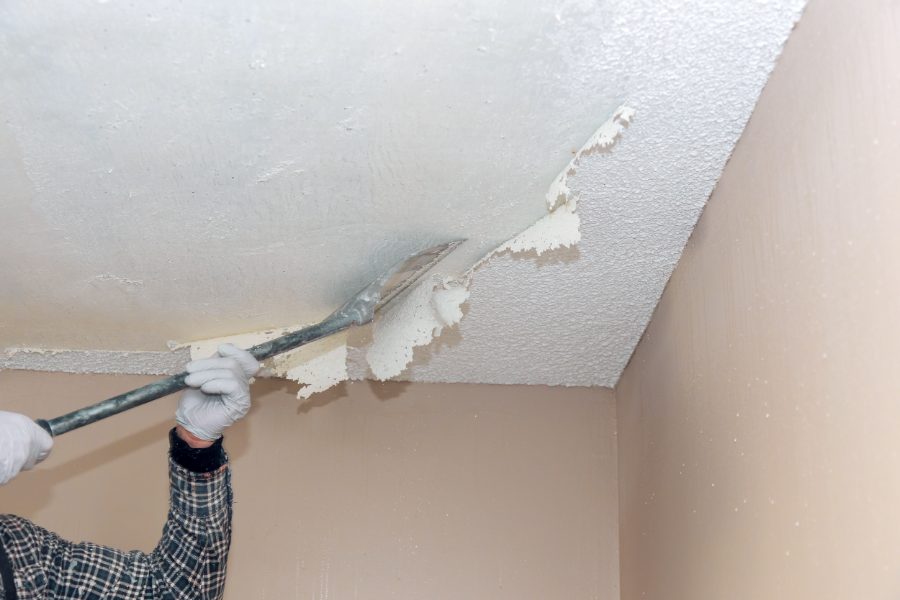 Popcorn ceiling being scraped smooth before painting