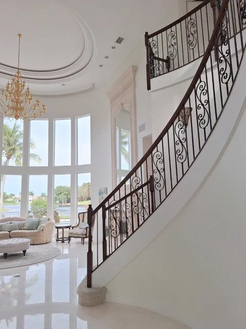 Curved stairwell with a dark iron railing against freshly painted white walls, with the window wall behind.